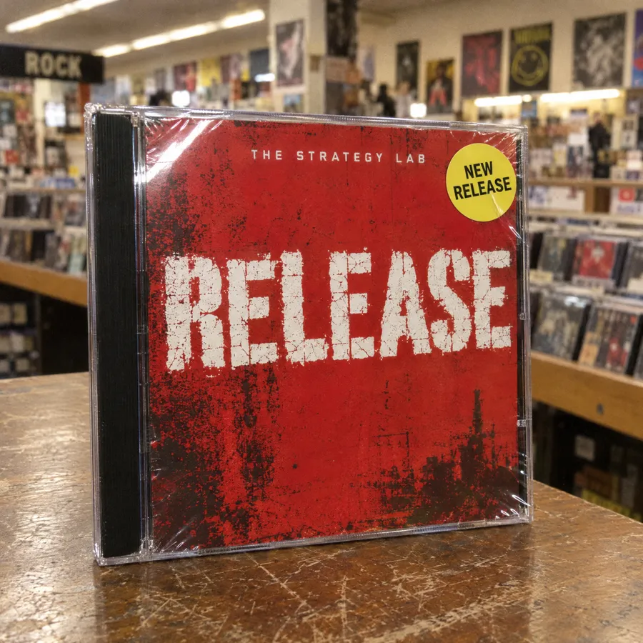A CD in its jewel case on a record store counter: red grunge cover titled Release, with a New Release sticker