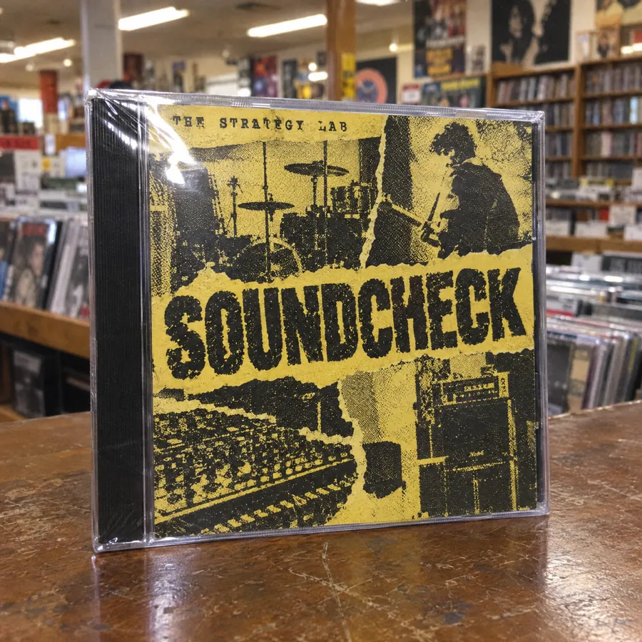 A CD in its jewel case on a record store counter: yellow photocopied collage cover titled Soundcheck